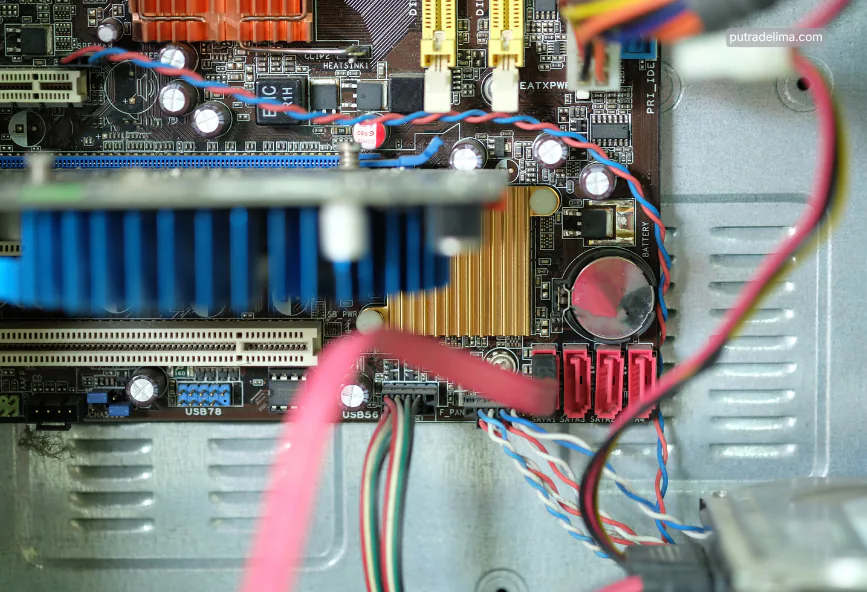 komponen motherboard komputer yang menampilkan kumpulan kapasitor elektronik kecil beserta heatsink dan kabel
