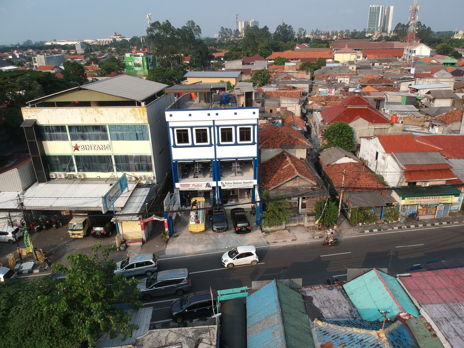 a city street scene with a car parked in front of a building gedung kantor putra delima mandiri